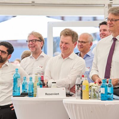 Mehrere Menschen stehen in einem Zelt. Im Vordergrund stehen Tische mit Getränken.