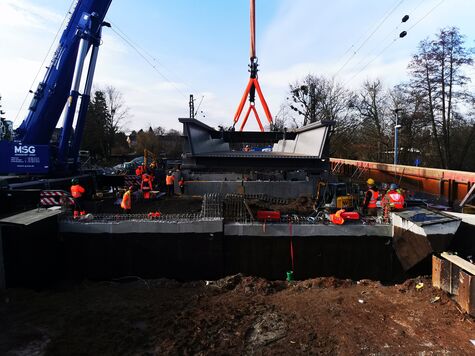 Bauarbeiter auf der Brückenkonstruktion schauen auf großes Bauteil der EÜ Salisbach, welches am Kran hängt