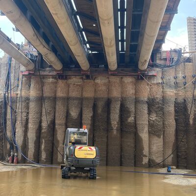 Baustelle unterhalb von Rohren mit kleinen Baggern auf überschwemmten Boden im Vordergrund