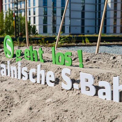 Ein Sandhaufen. Darauf stehen Buchstaben Es geht los. Nordmainische S-Bahn.