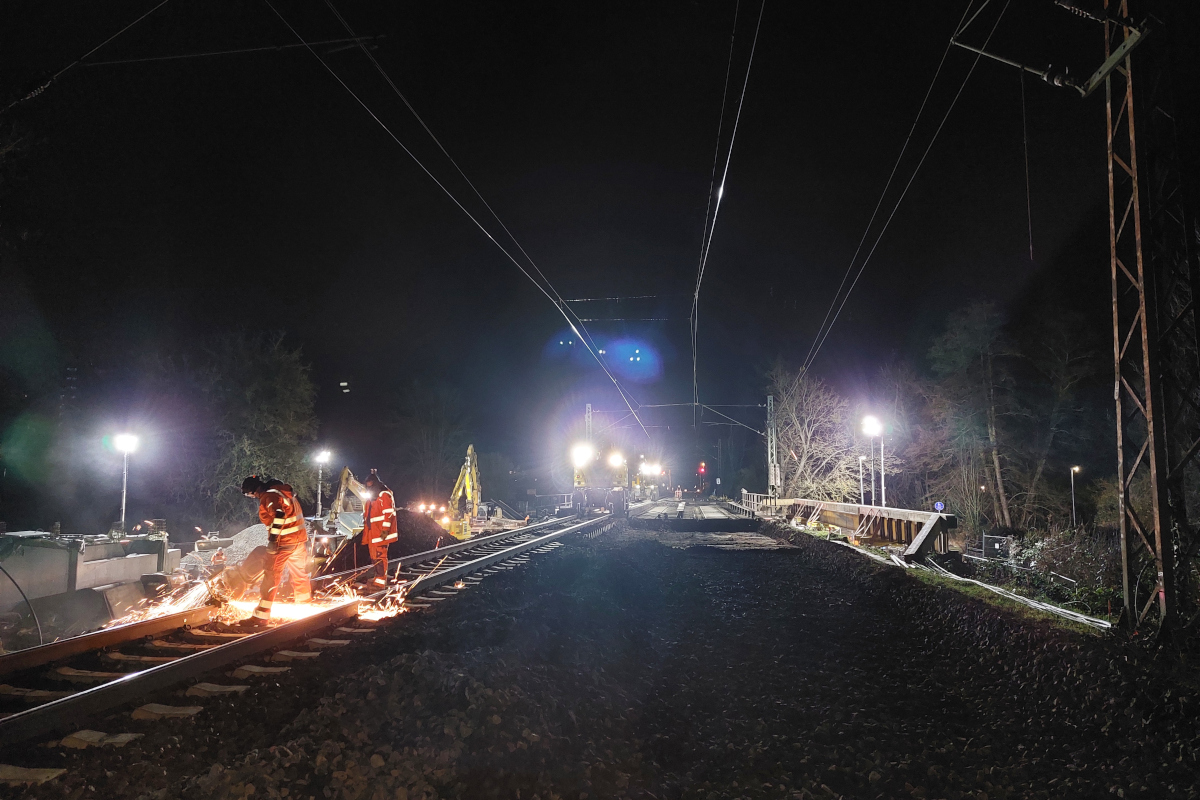 Rechts im Bild zerschneidet ein Mitarbeiter die Schienen auf der Brücke mithilfe eines Trennschleifers bei Nacht. Dabei fliegen Funken.